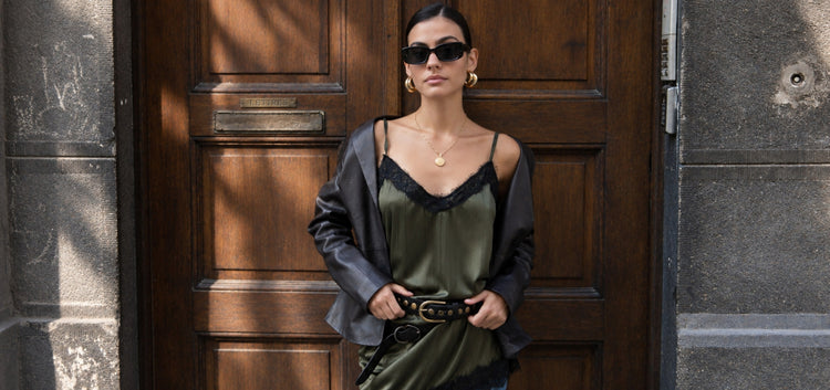 Woman in a leather jacket and olive slip dress wearing an Amsterdam Heritage studded leather belt in a doorway