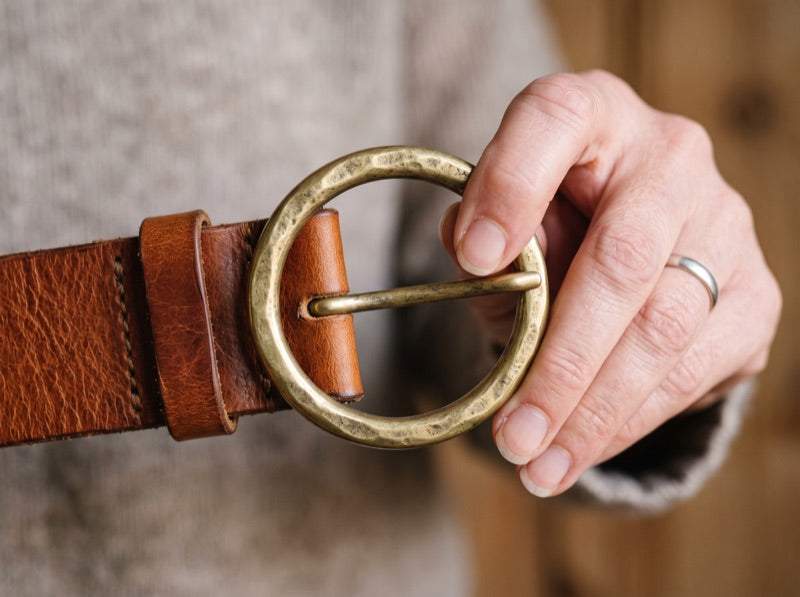 A round metal buckle held between finger and thumb